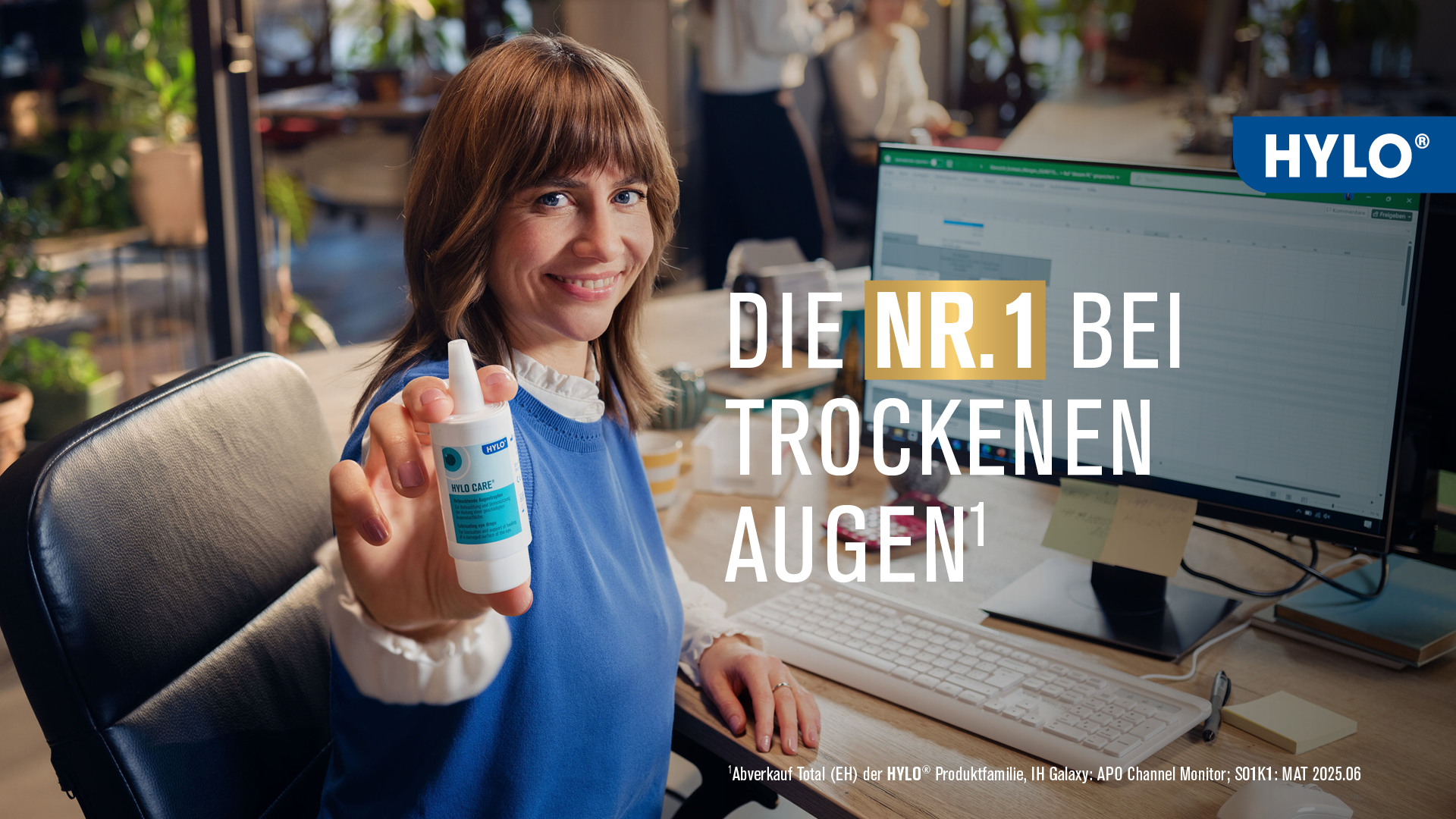 Eine Frau sitzt an ihrem Bildschirmarbeitsplatz im Büro. Sie hält eine Flasche Augentropfen (HYLO®-CARE der Firma URSAPHARM) in die Kamera. Daneben steht der Claim: HYLO® DIE NR.1 BEI TROCKENEN AUGEN
