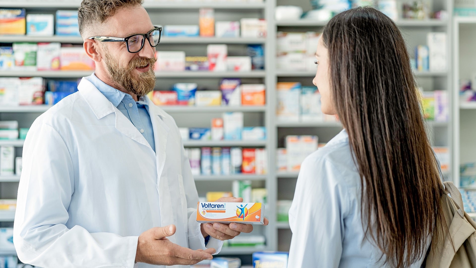 Apotheker reicht einer Kundin eine Packung Voltaren