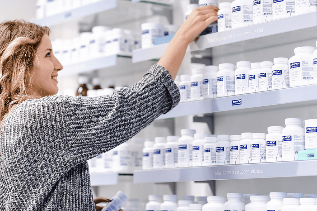 Junge Frau nimmt Pure Encapsulations Produkt aus Regal.